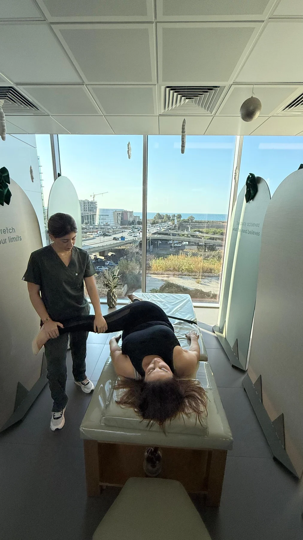 A therapist guiding a stretch in the clinic’s sunlit treatment room